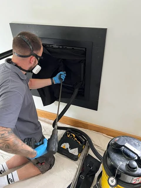 Technician cleaning a modern residential fireplace with vacuum equipment