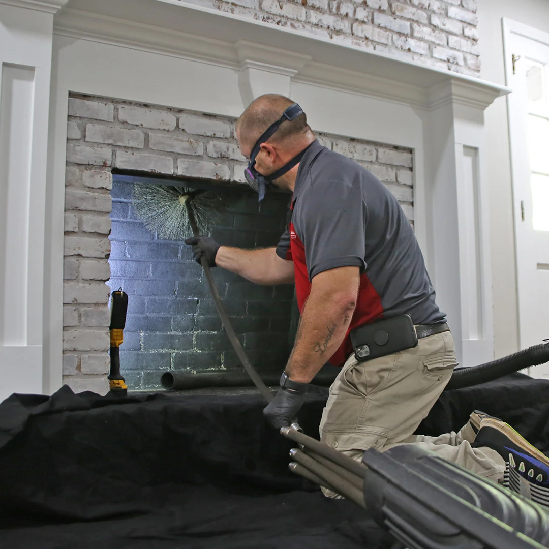 Chimney technician brushing the interior of a residential brick fireplace